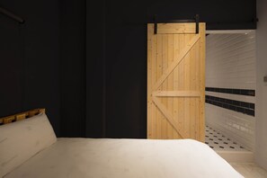A bedroom with a wooden door, a white bed, and a tiled shower area. - Birdeye Garden (Tainan)