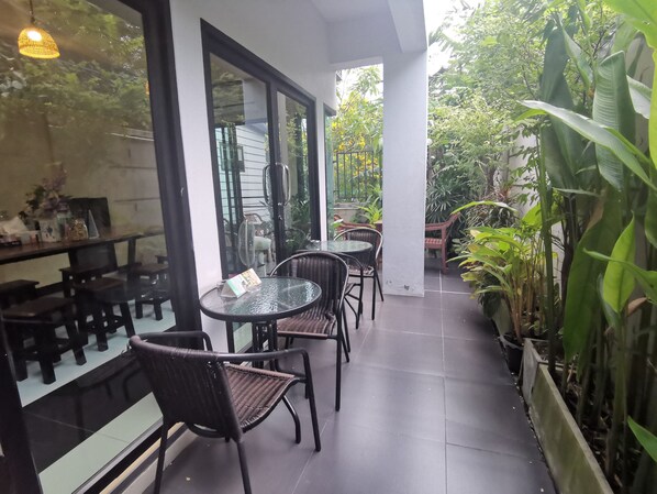 An outdoor seating area with tables and chairs, surrounded by potted plants and a glass wall. - Hide Bangkok Hostel (Bangkok)