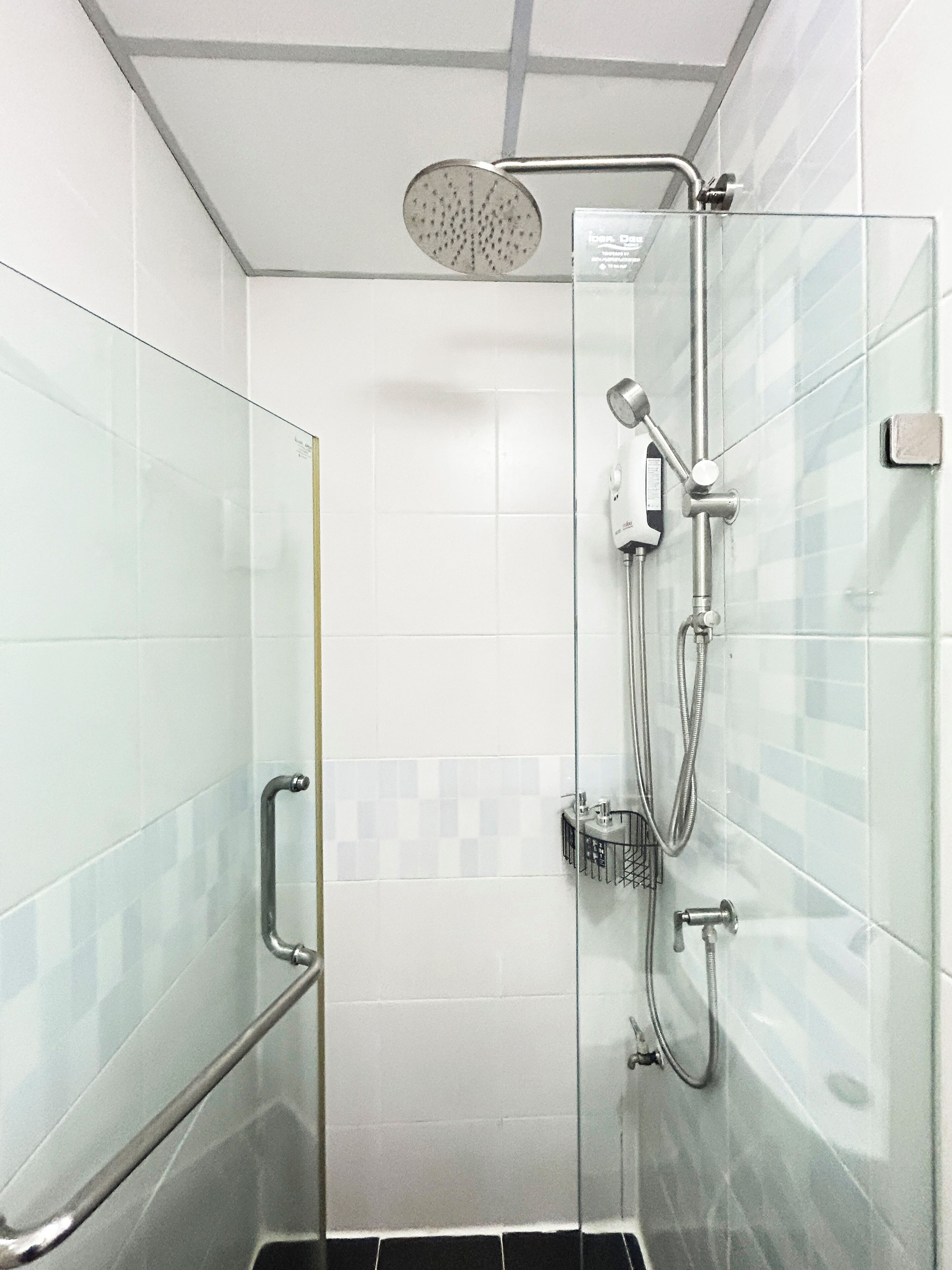 A glass-enclosed shower stall with a handheld showerhead, a handheld shower attachment, and a wall-mounted faucet.
