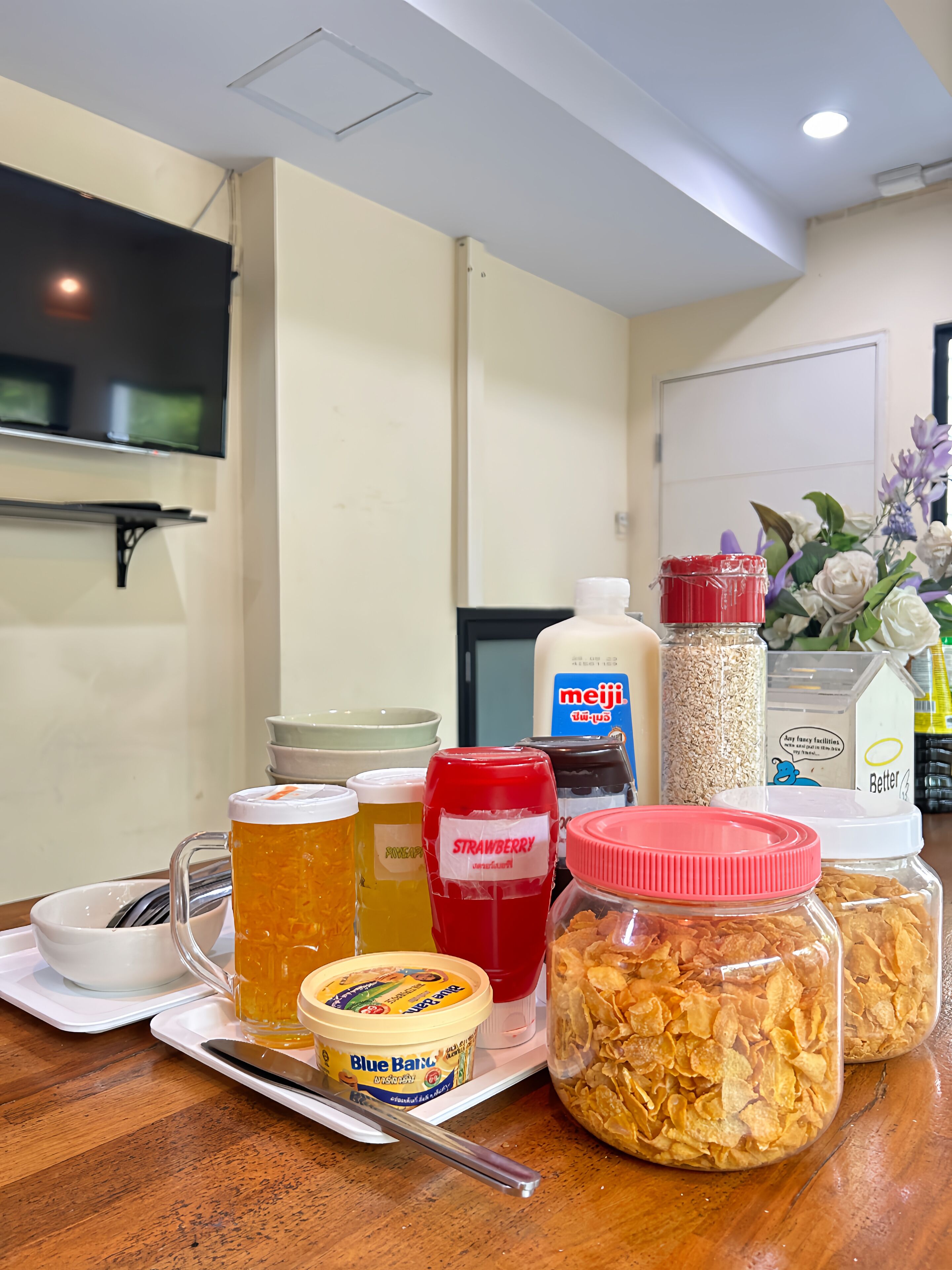 A kitchen counter with various food items and beverages, including a jar of cereal, a container of milk, and a bottle of strawberry jam.