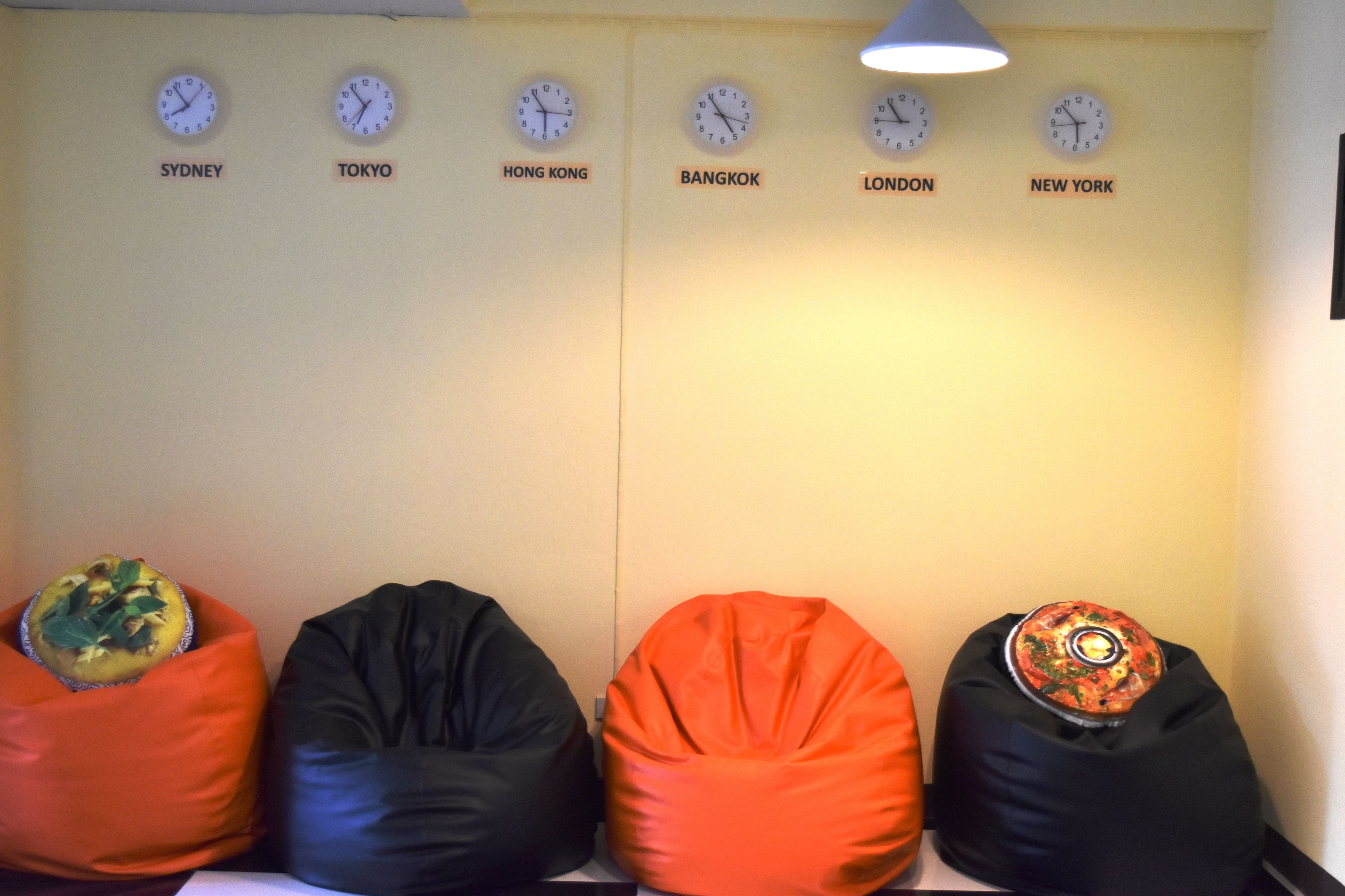 A wall with clocks labeled with city names and bean bags with decorative pillows.