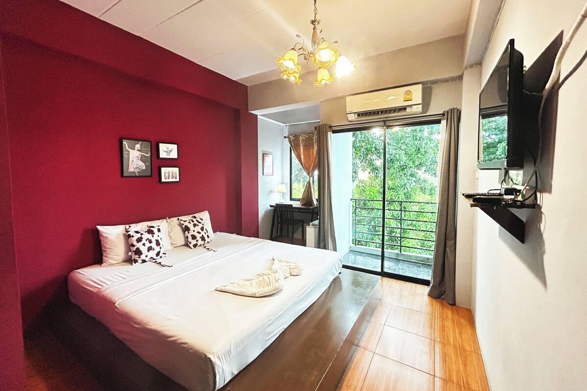 Une chambre à coucher avec un lit, un téléviseur fixé au mur et une porte-fenêtre coulissante donnant sur un balcon.