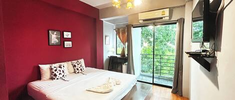 A bedroom with a bed, a TV mounted on the wall, and a sliding glass door leading to a balcony.