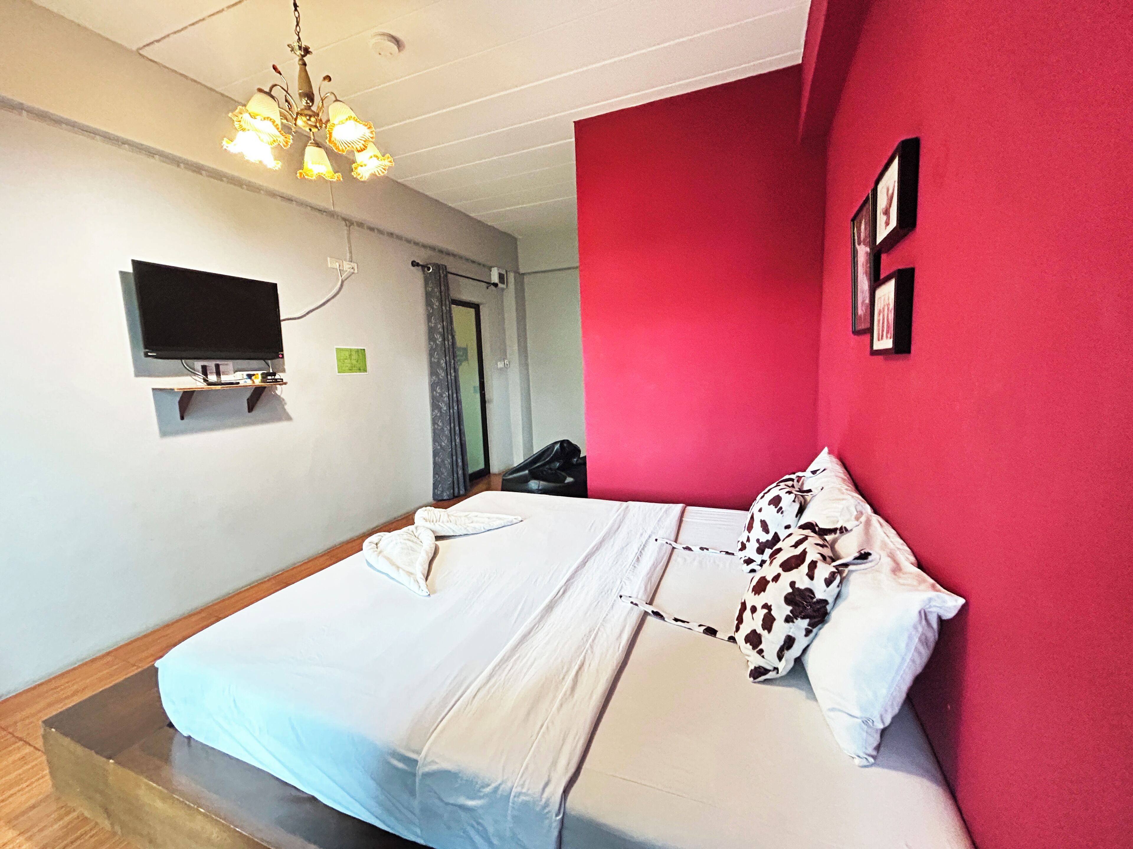 A bedroom with a bed, a television mounted on the wall, and a red accent wall.