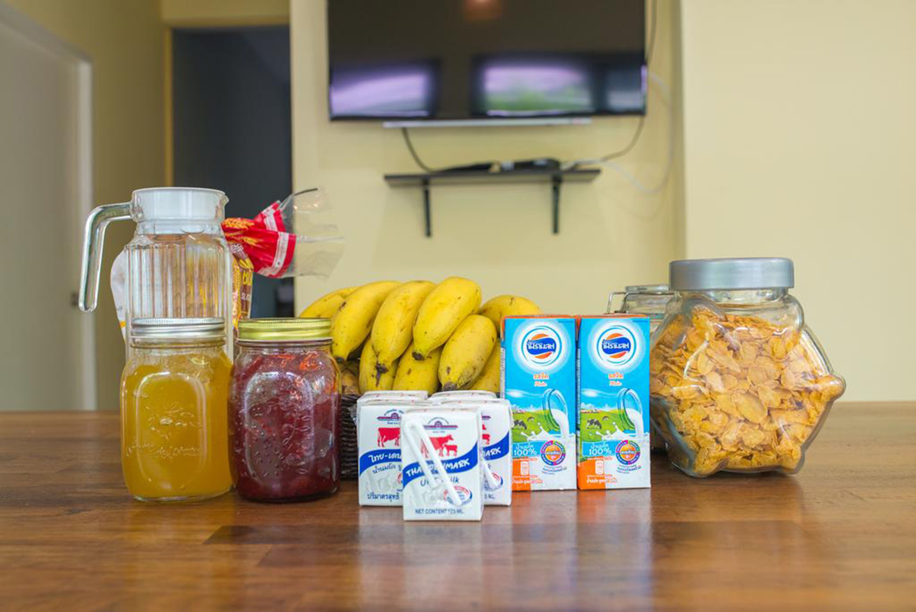 Un plan de travail de cuisine avec une carafe, des pots de confiture, des bananes, des produits laitiers et des boîtes de céréales.