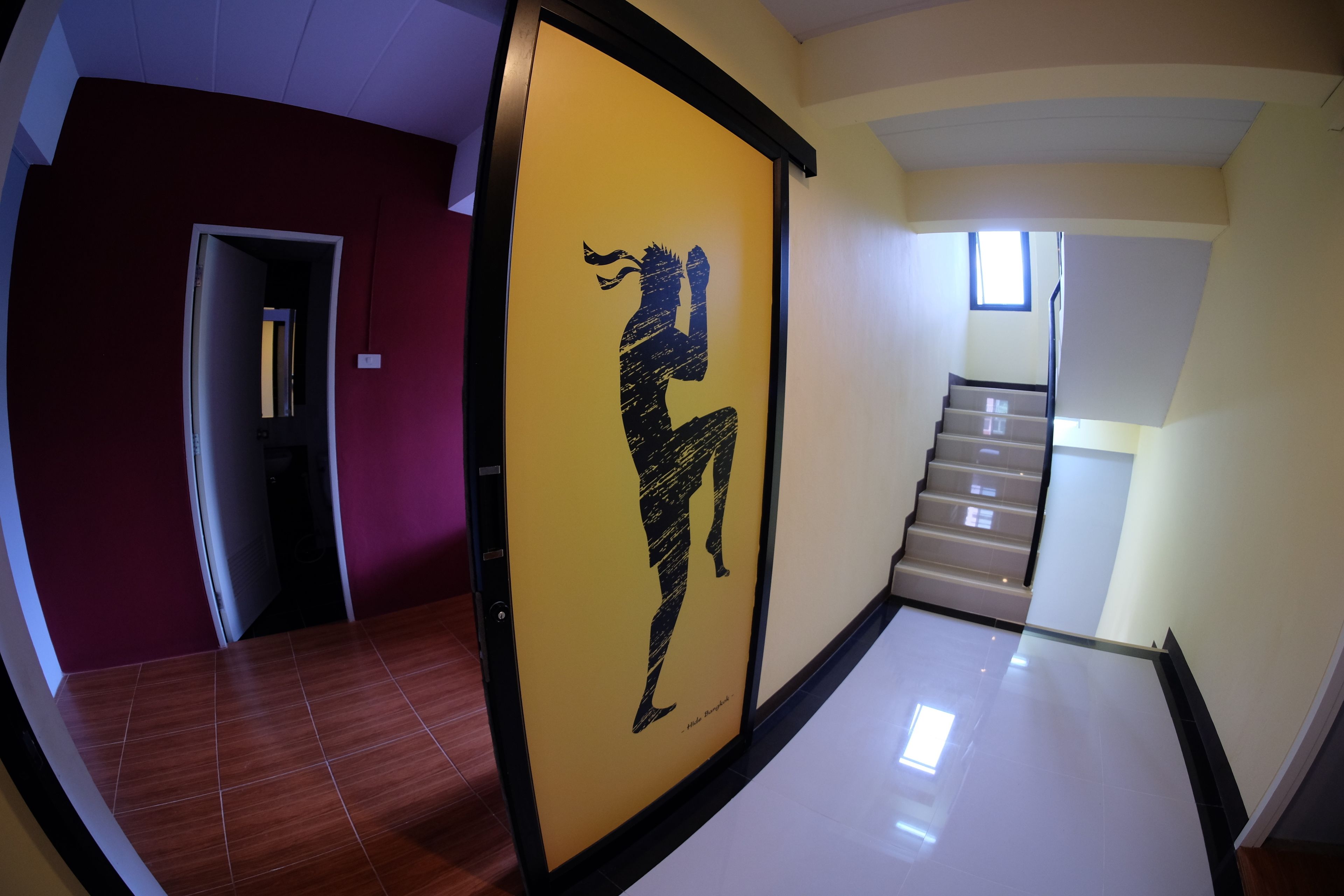 A hallway with a yellow framed artwork of a person in a dynamic pose, a staircase with beige steps, and a red wall on one side.
