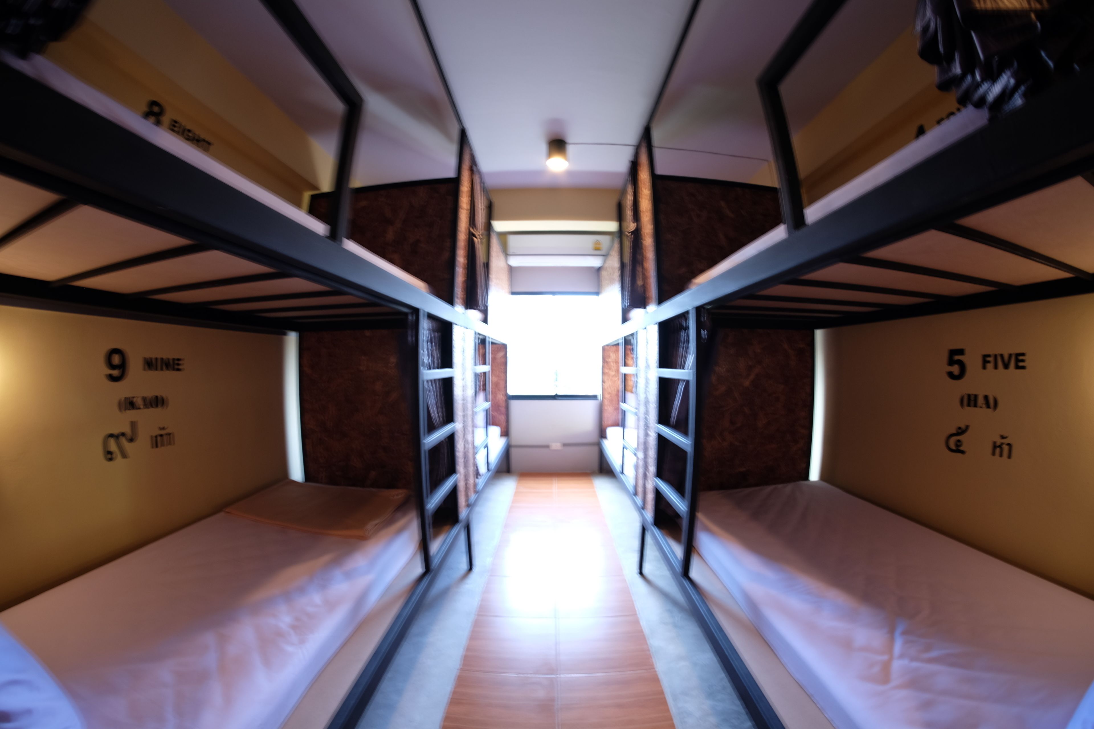 A narrow corridor with bunk beds on either side, labeled with room numbers and names.