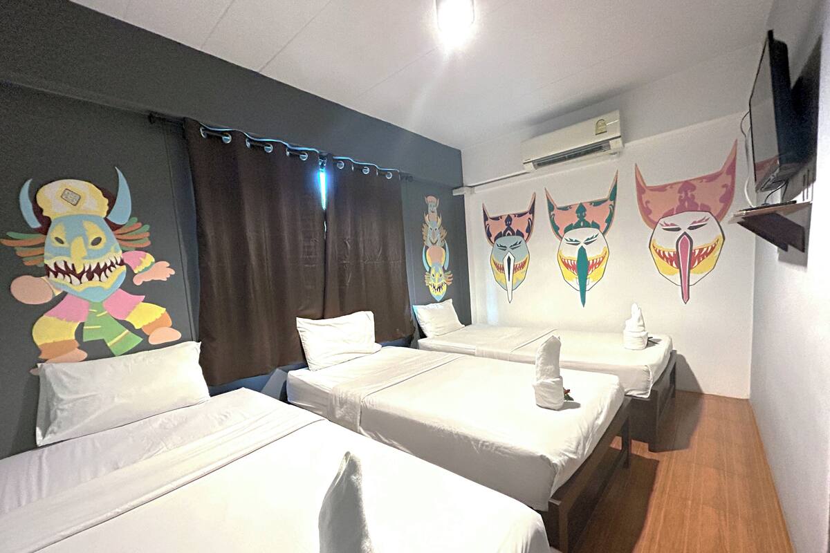 Une chambre d’hôtel avec trois lits simples, un mur décoré de masques colorés et un appareil de climatisation.