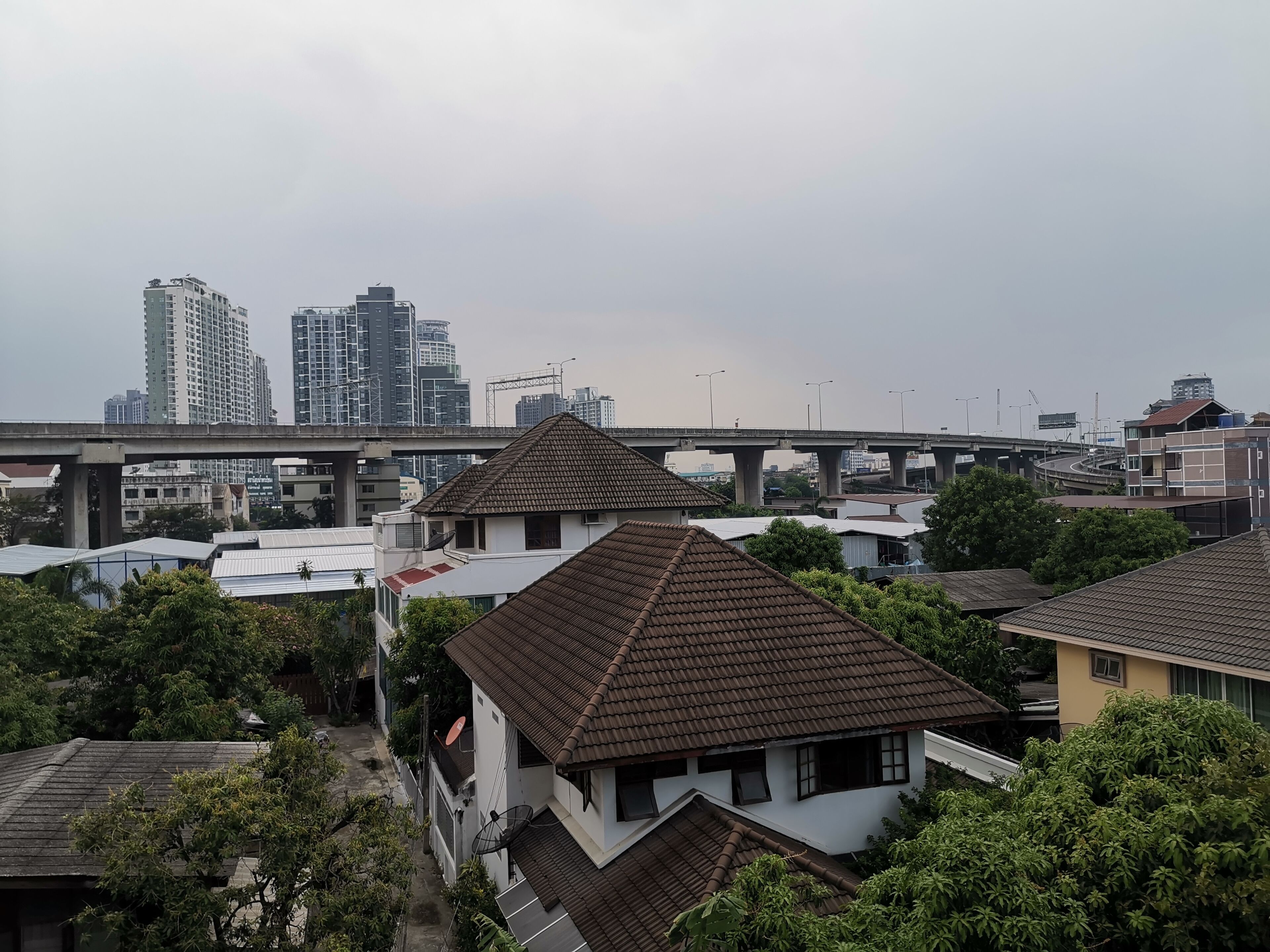 A residential area with traditional houses, a bridge, and high-rise buildings in the background.