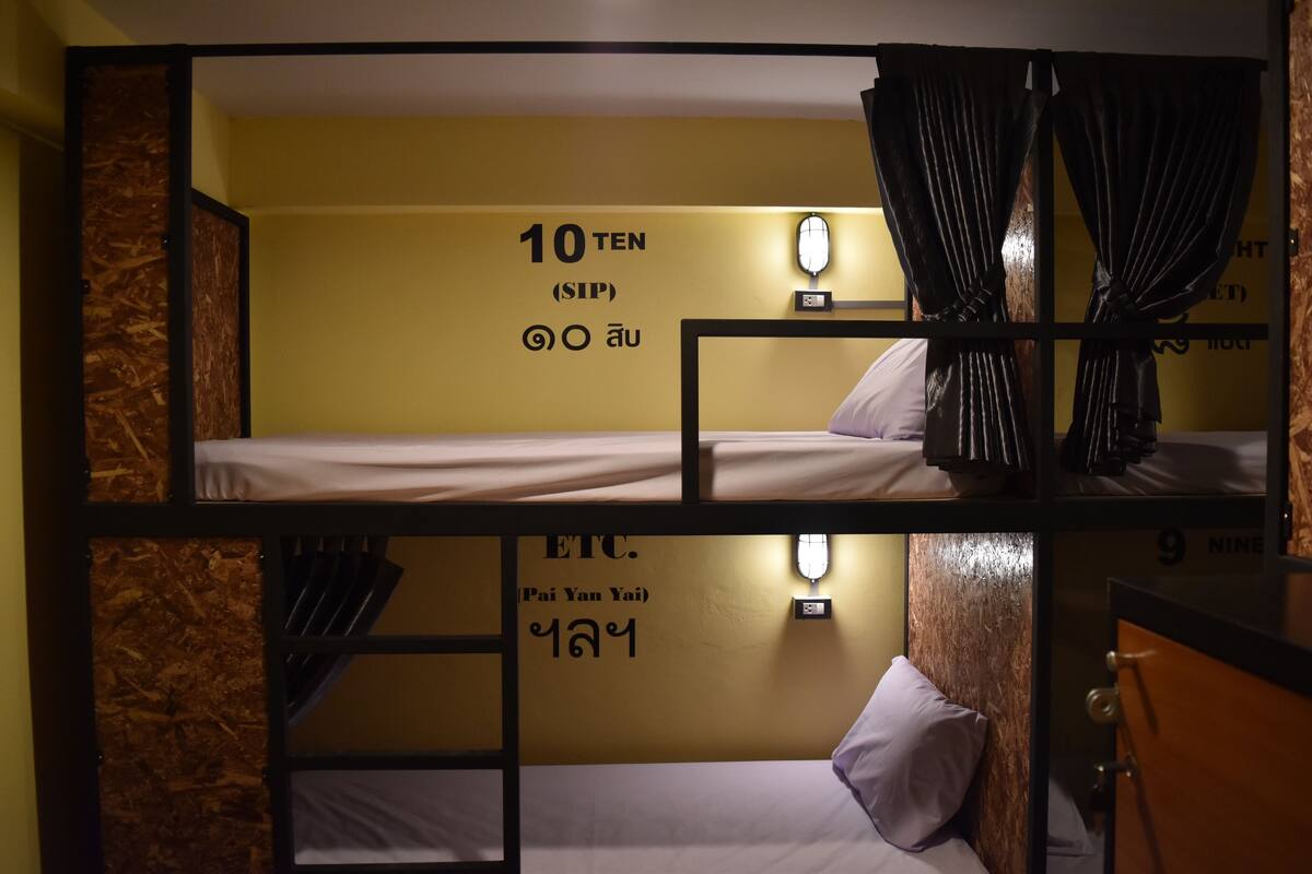 Une chambre avec un lit superposé, un mur jaune, une horloge murale et une fenêtre avec des rideaux.