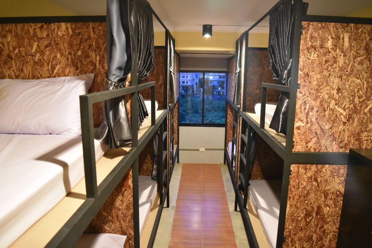 Une chambre avec deux lits superposés, des murs en bois et une fenêtre donnant sur des immeubles.