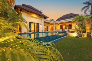 Ein modernes Haus mit Swimmingpool, Sitzgelegenheit im Freien und tropischen Pflanzen.