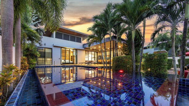 A modern house with a glass-enclosed pool, surrounded by palm trees and a sunset view. - Baan Bua Estate by Tropiclook (Rawai)