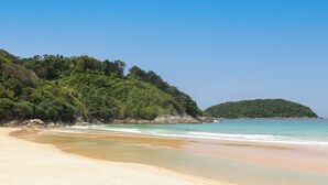 A beach with clear turquoise water, sandy shore, and a forested hill in the background. - Baan Bua Estate by Tropiclook (Rawai)
