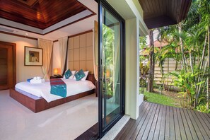 Een hotelkamer met een groot bed, een glazen deur naar een balkon en uitzicht op tropische begroeiing.
