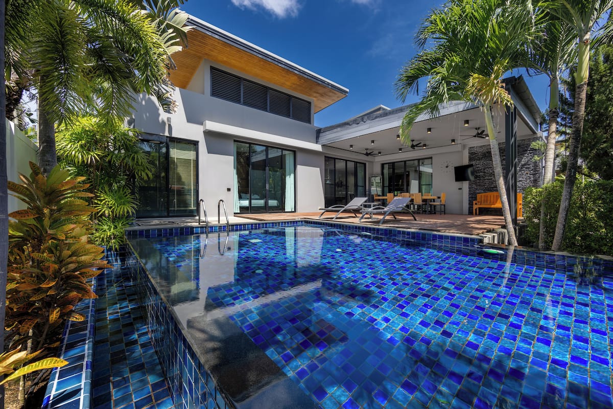 Una casa moderna con piscina, ventanas amplias y mobiliario exterior.