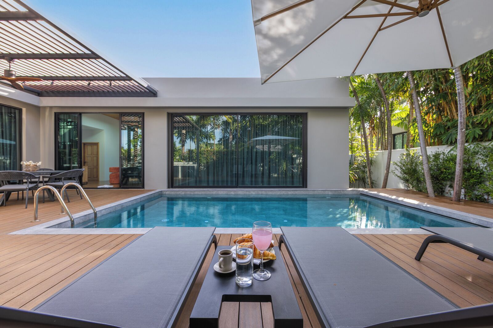 A modern pool area with a lounge table, chairs, and a glass of drink.