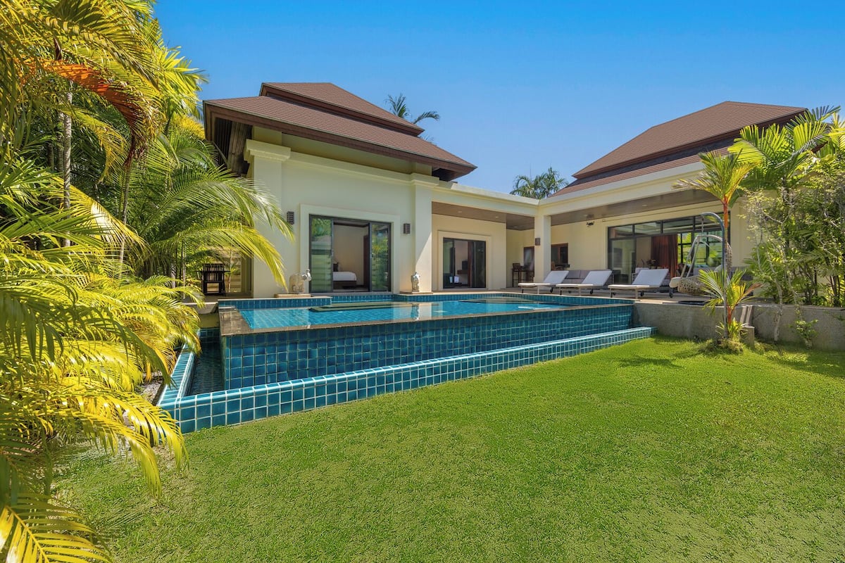 Una casa moderna con piscina, dos balcones y exuberante vegetación.