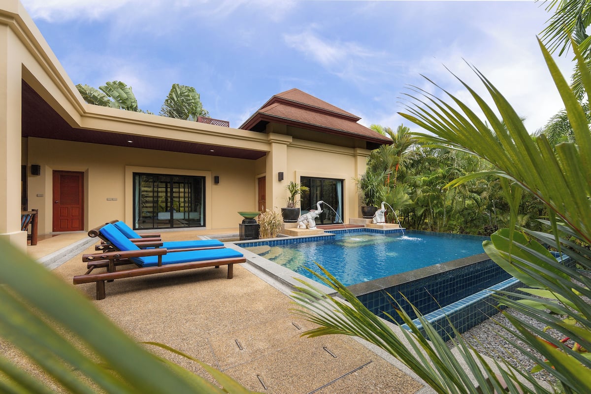 Una casa moderna con piscina, sillones de descanso y plantas tropicales.