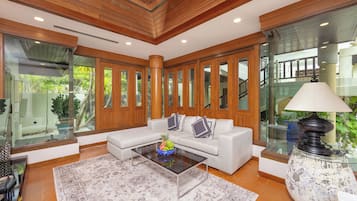 Uma sala de estar moderna com um sofá branco, mesa de centro de vidro e uma luminária decorativa.