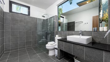 Une salle de bain moderne avec une douche à parois de verre, des toilettes blanches et un grand miroir au-dessus du lavabo.