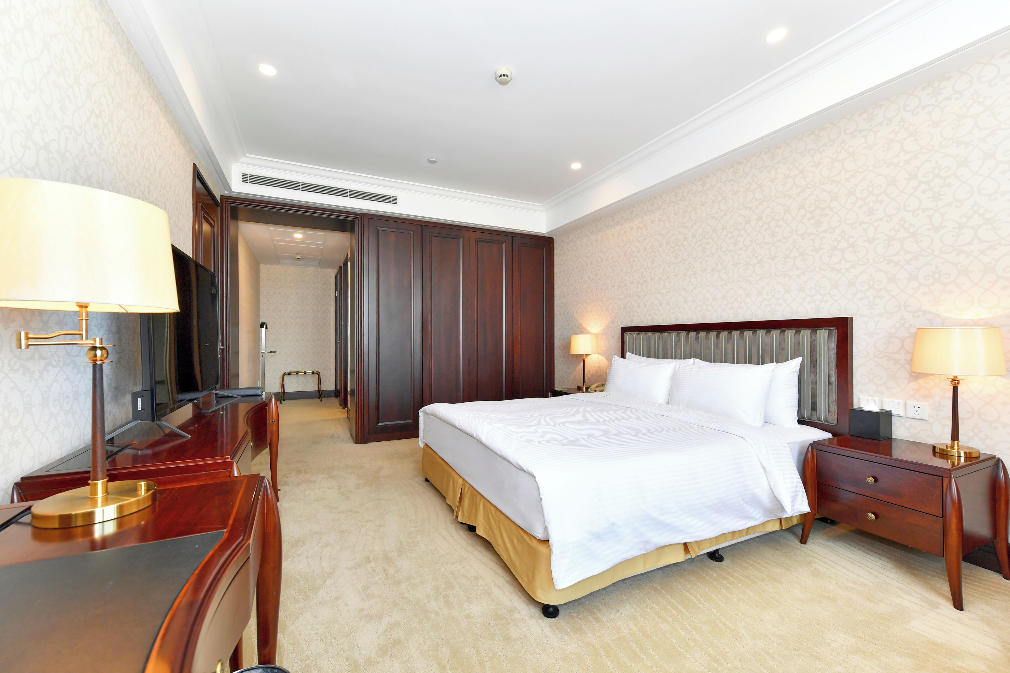 A hotel room with a large bed, wooden nightstands, a desk, and a chair.