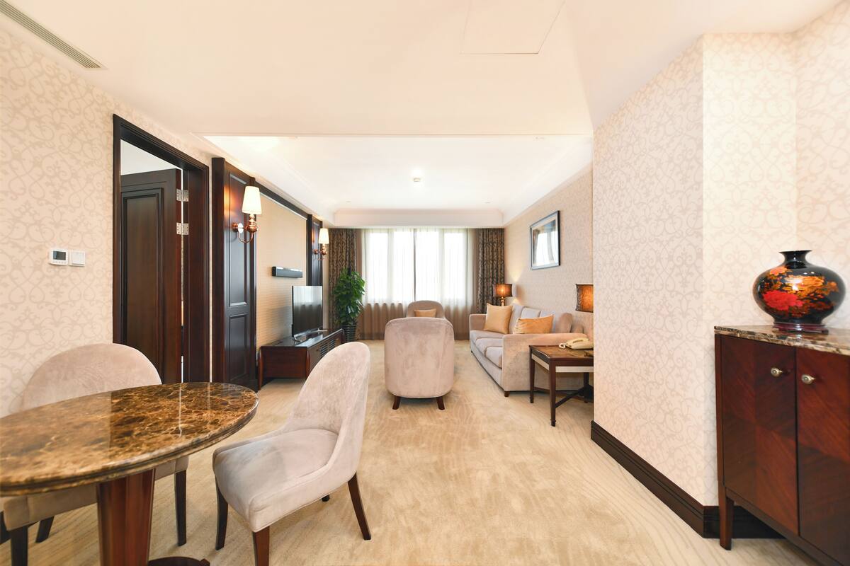 Een hotelkamer met een eethoek, een bank, een televisie en een decoratieve vaas.