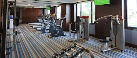 A gym with treadmills, dumbbells, and a TV screen displaying a soccer game.