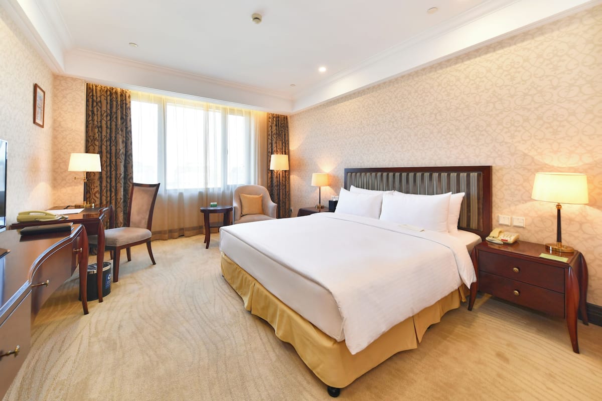 Een hotelkamer met een groot bed, een bureau met stoel, een klein tafeltje en twee lampen.