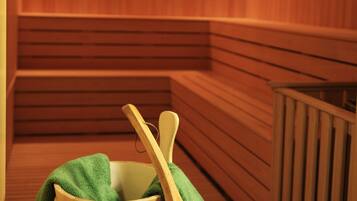 Un sauna en bois, avec des bancs et un récipient en bois contenant une serviette verte et une louche en bois.