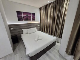 Una habitación de hotel moderna con una cama grande, cabecera con diseño texturizado y un conjunto de tres cuadros en la pared.