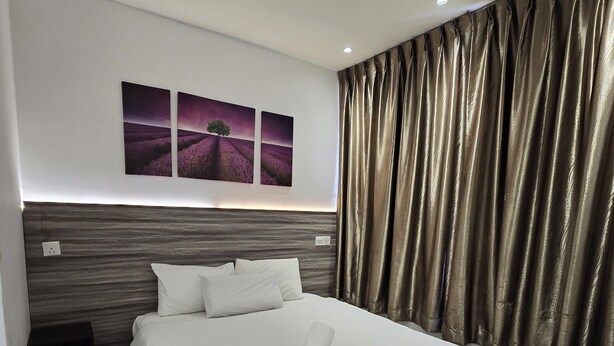 A modern hotel room with a large bed, a headboard with a wood-like texture, and two wall-mounted paintings of a purple landscape. - One Point Hotel - RH Plaza (Kuching)