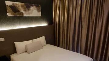 A hotel room with a large bed, a headboard with a decorative panel, a wall-mounted light, and a window with curtains.