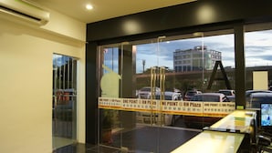 A modern hotel lobby with glass doors, a reception desk, and a view of parked cars and buildings outside. - One Point Hotel - RH Plaza (Kuching)