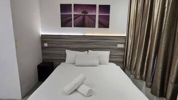 Una habitación de hotel moderna con una cama grande, un cabecero con televisor integrado y un cuadro sobre la cama.