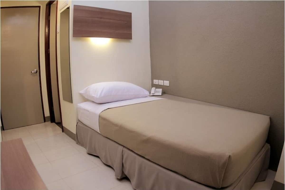 A single bed with a beige bedspread and white pillow in a room with a wooden headboard and a wall-mounted phone.