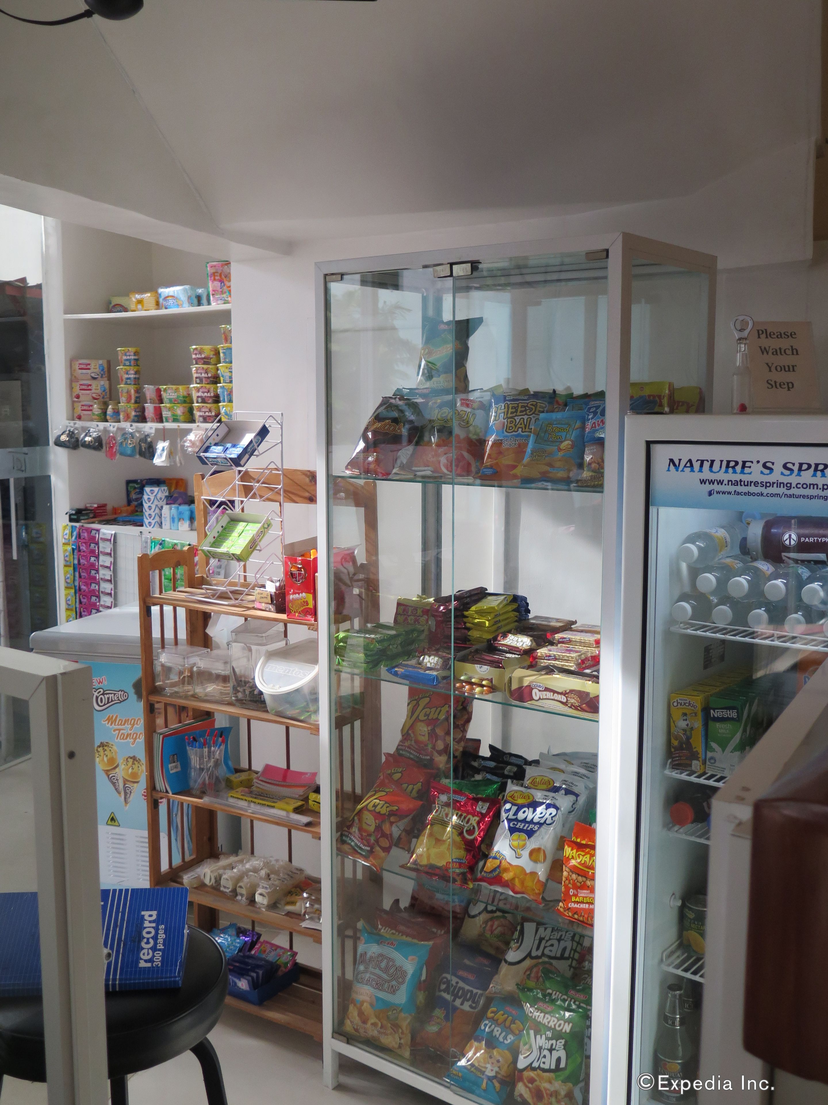 Interior de una tienda con estantes llenos de bocadillos, un refrigerador con agua embotellada y un cartel de Nature's Spring.