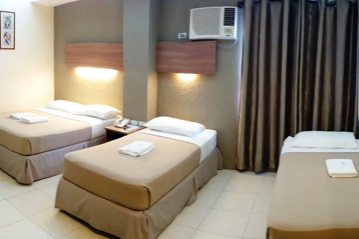 A hotel room with two single beds, a small table, an air conditioning unit, and a curtain.