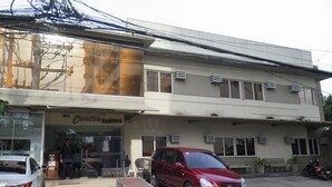 Un edificio con un letrero que dice 'The Center Suites' hotel. Hay dos coches estacionados adelante, un sedán blanco y un SUV rojo.