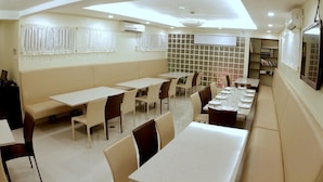Un comedor con varias mesas y sillas, un techo alto con iluminación empotrada y un amplio ventanal con cortinas.