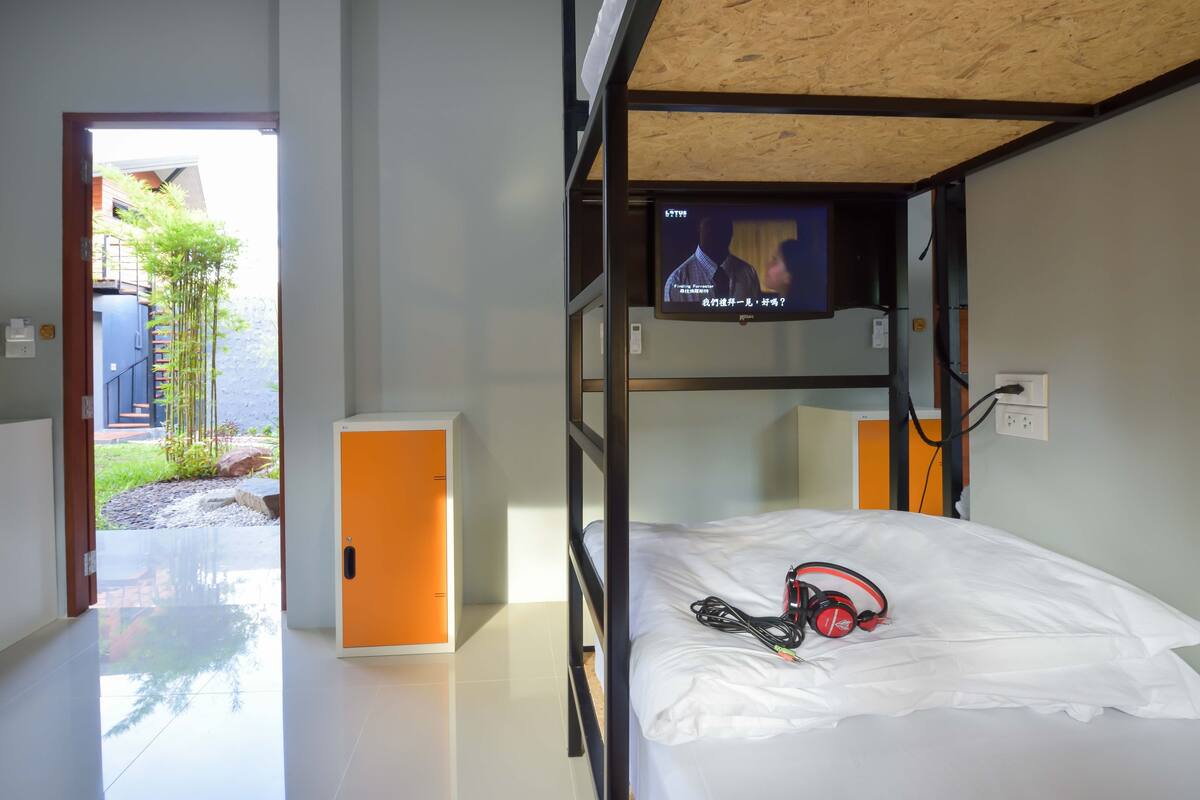 A bunk bed room with a television on the wall, a pair of headphones on the bed, and a view of the outside.