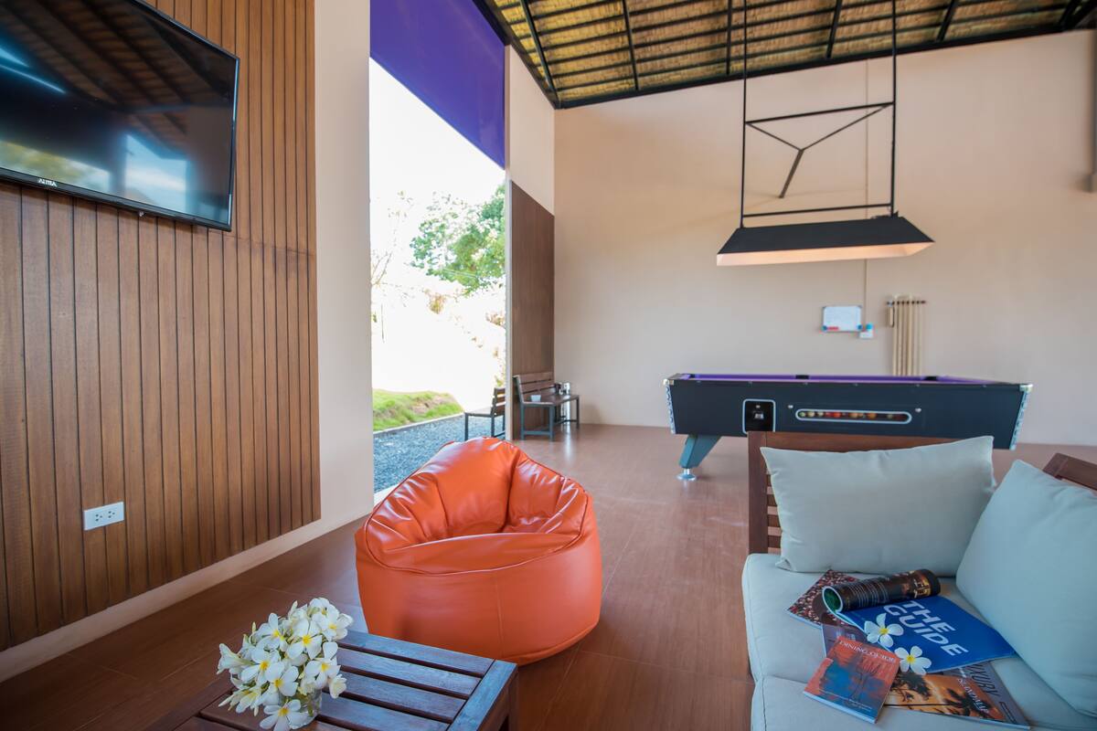 A modern living room with a pool table, orange bean bag, and a sofa with magazines.