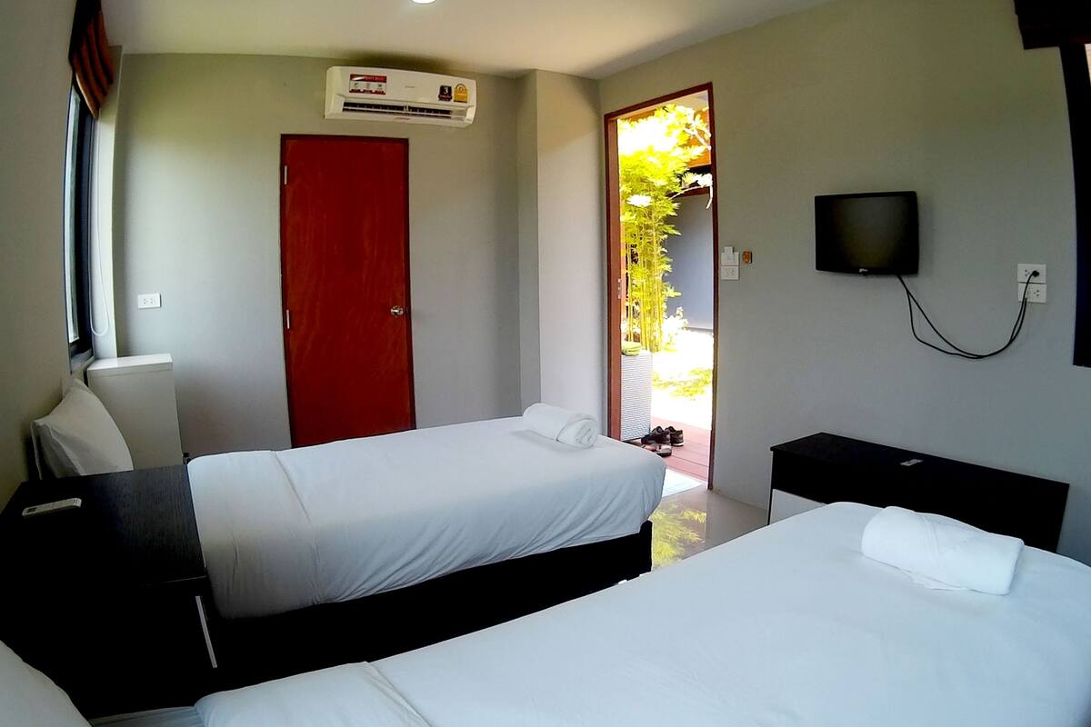 A hotel room with two beds, a TV, and an air conditioning unit.