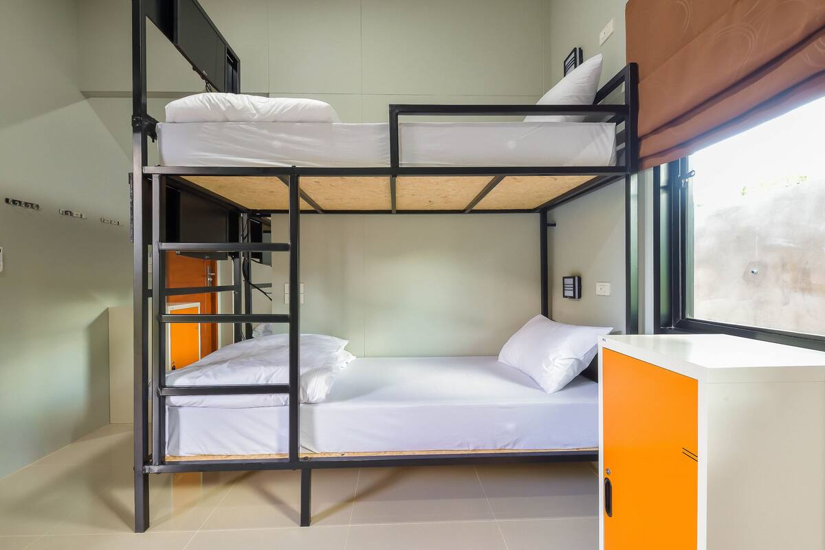 A bunk bed room with a window, a desk, and a cabinet.