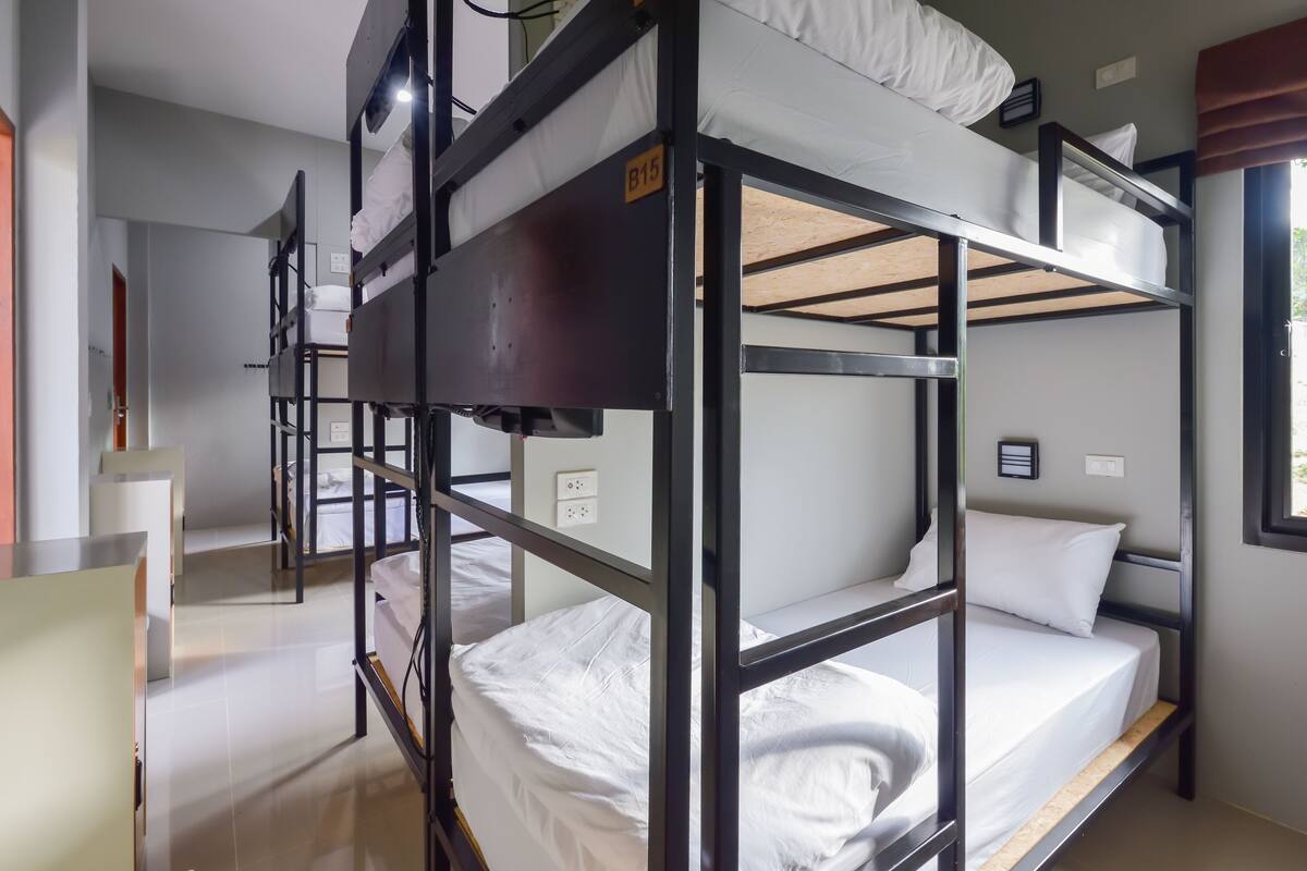 A bunk bed room with a visible electrical outlet and a window with curtains.