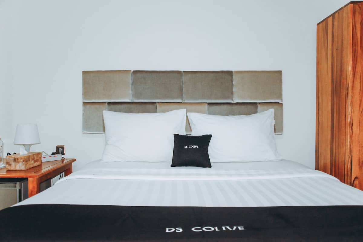 A hotel room with a bed, a wooden nightstand, a lamp, and a wardrobe.