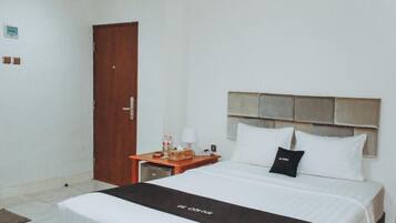 Een hotelkamer met een bed, een houten nachtkastje, een lamp en een deur.