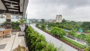Un balcon doté d’un espace repas, offrant une vue sur le paysage urbain et donnant sur une route bordée de verdure.