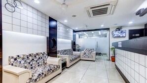 Un espace d’accueil moderne comprenant un comptoir de réception, un coin salon avec des canapés à motifs et un grand miroir.