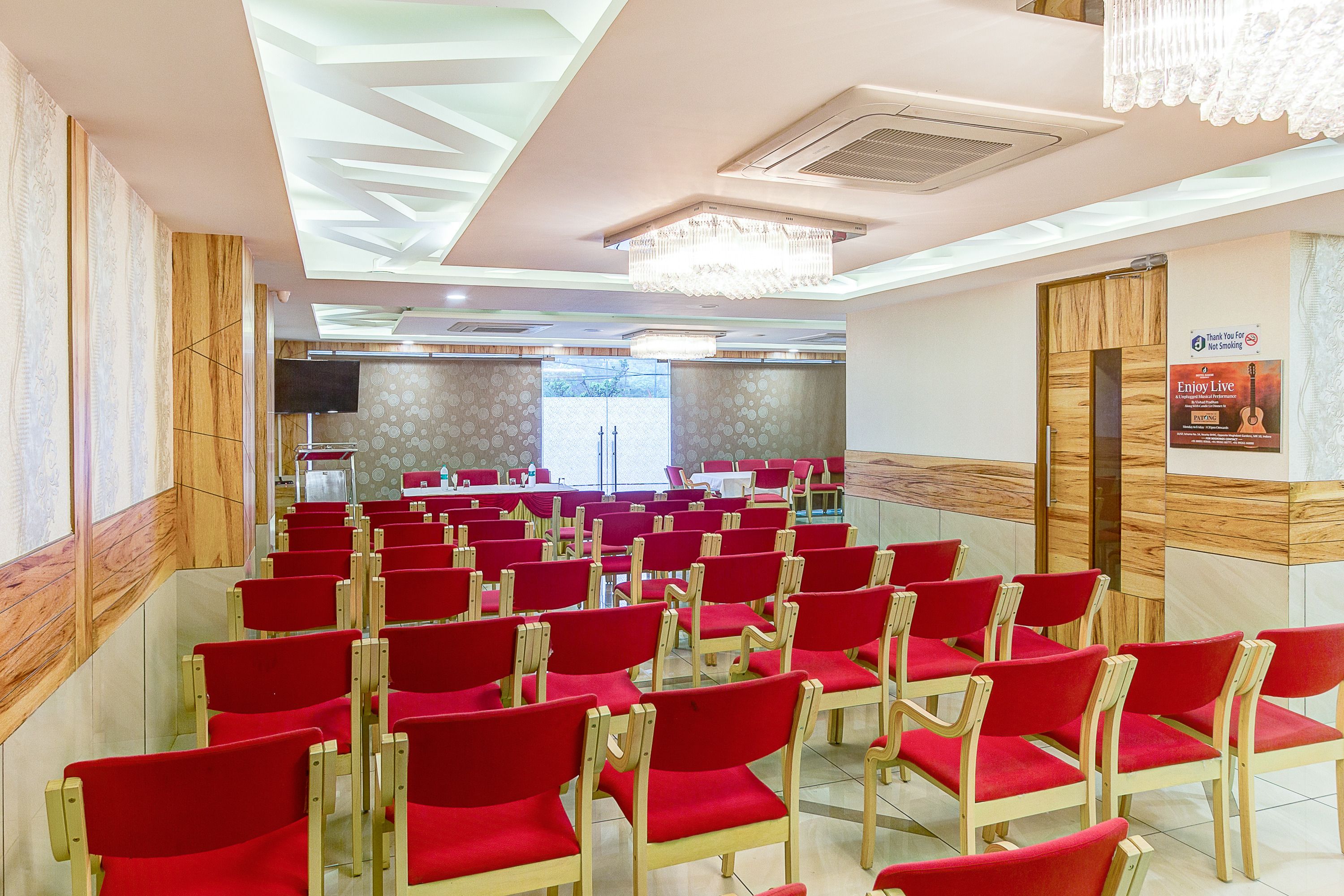 A conference room with rows of red chairs, a chandelier, and a wooden panel wall.